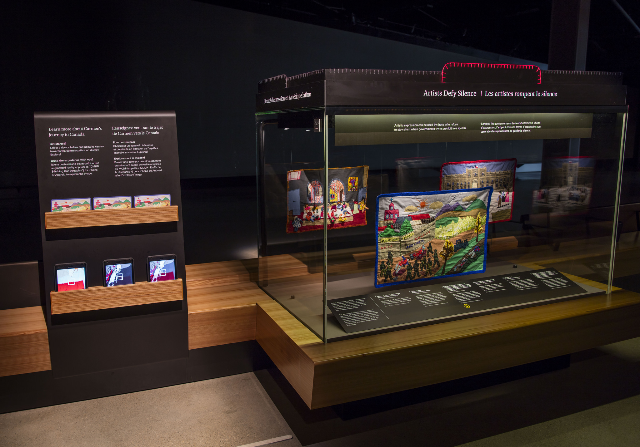 Rectangular glass case connected to a wooden bench. Attached is a vertical stand with racks of postcards and iPad minis.