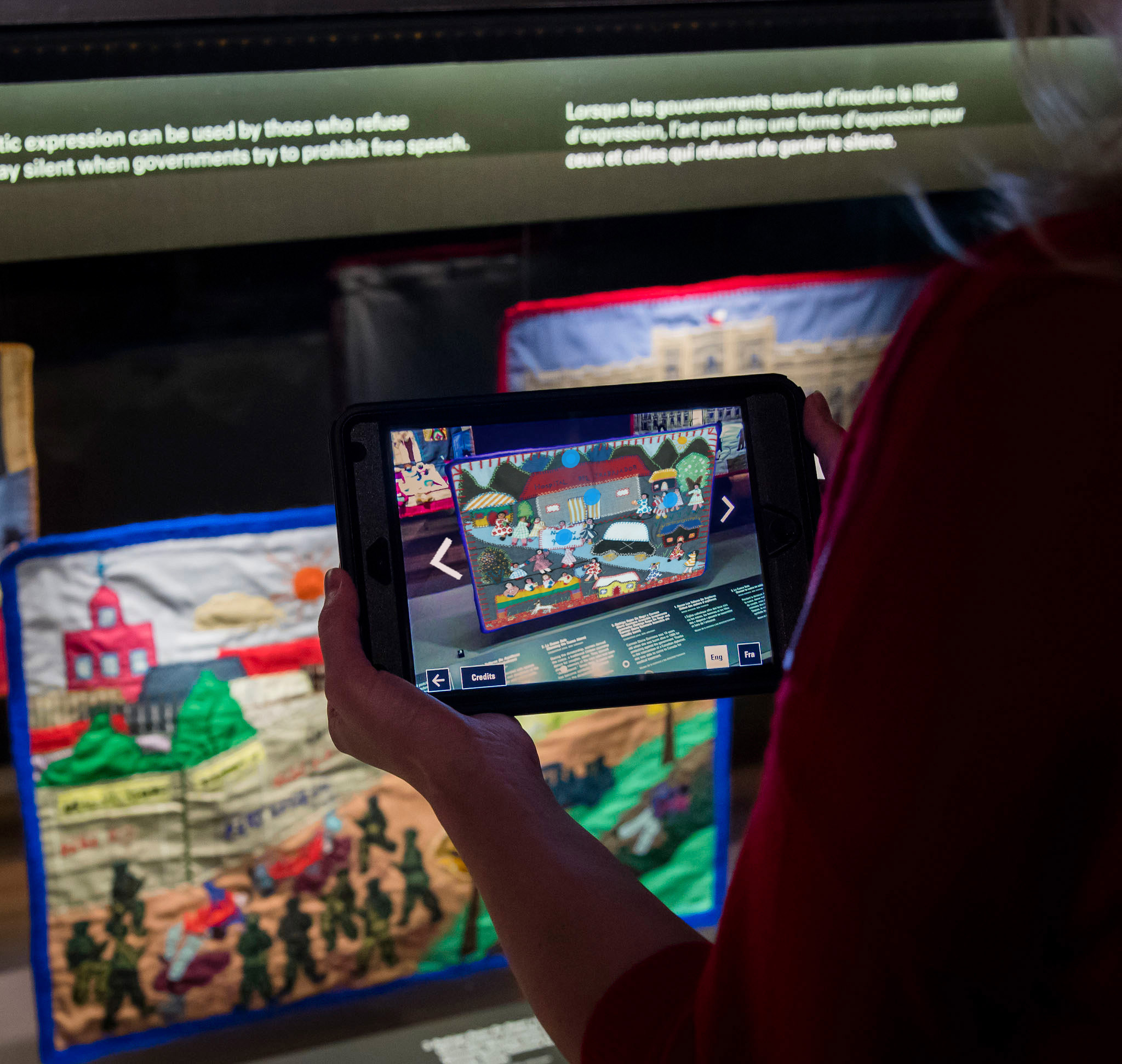 Two hands holding an small touchscreen in front of a rectangular glass case.