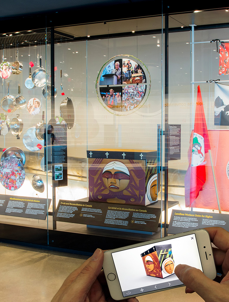 Glass case containing a wooden box in the background. Two hands holding a mobile phone in front of it with the app on screen.