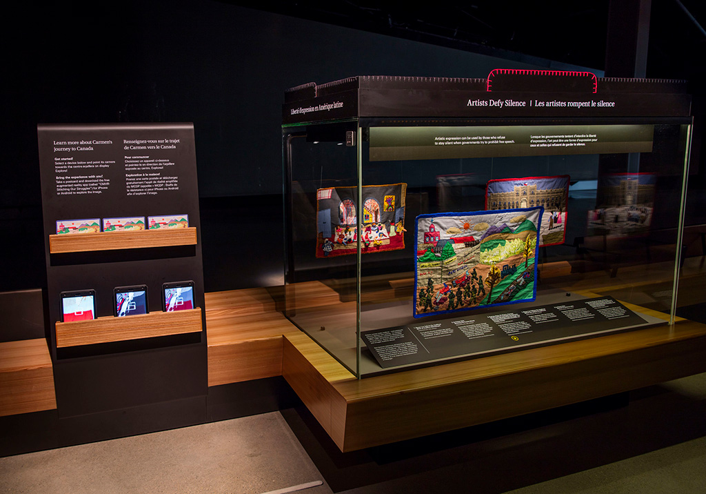 Metal stand with postcards and 3 tablets beside a large glass display case.
